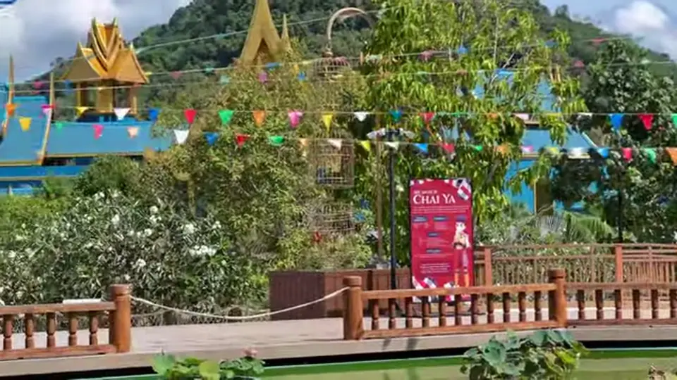 Boardwalk with bunting, trees, and blue-gold rooftops near a hillside.
