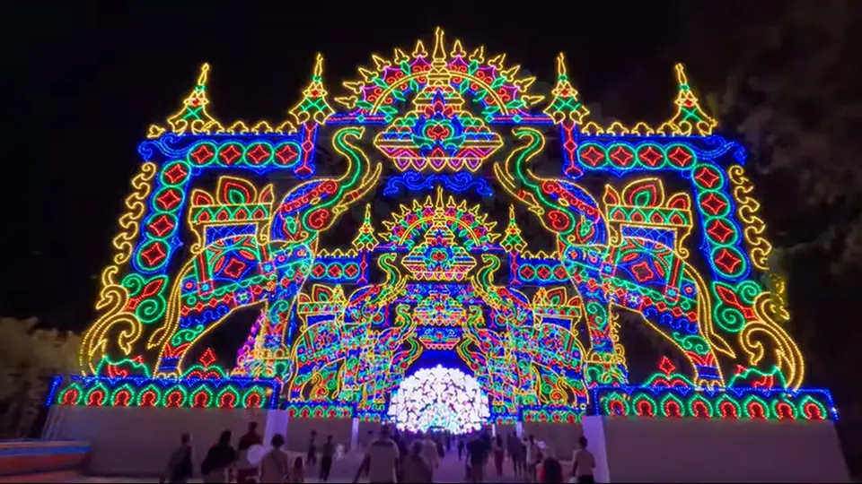 Visitors walk toward a giant illuminated elephant arch at night.