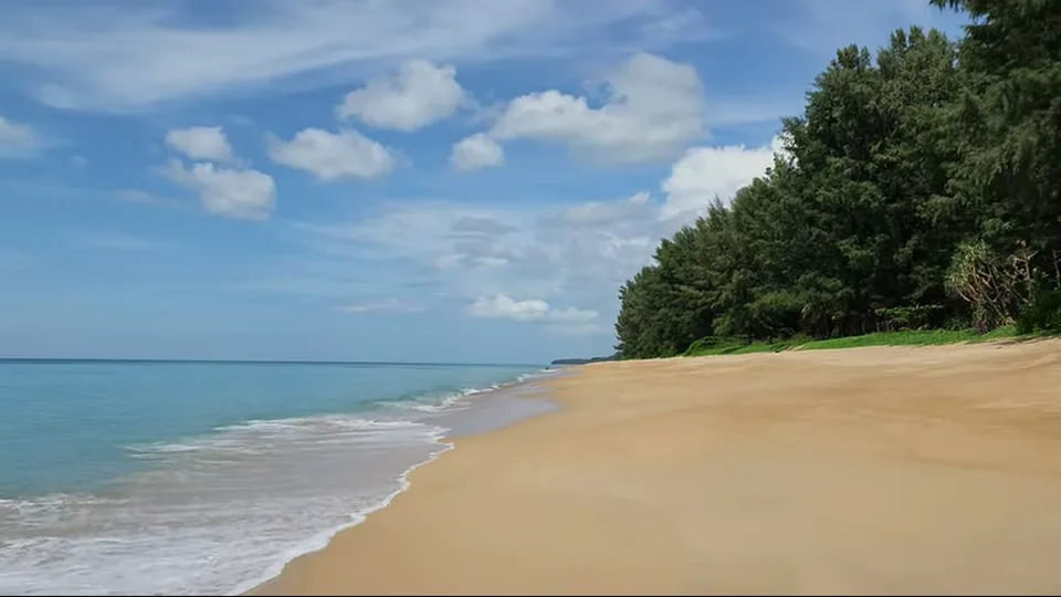 Red airplane flying low over the sea beside Mai Khao Beach